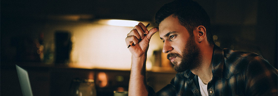 Photo of a stressed man sitting in kitchen late at night checking and paying bills