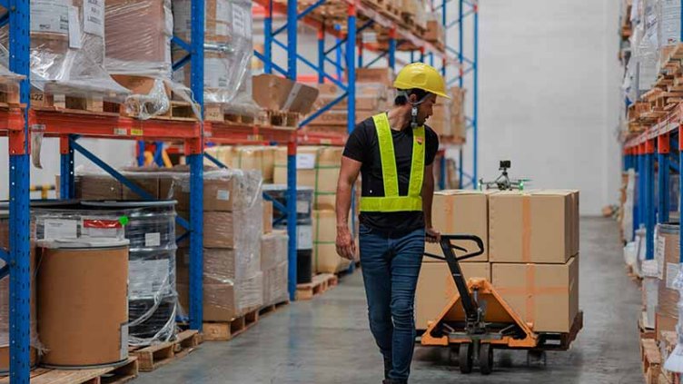 A man pulling a trolley of boxes in huge warehouse